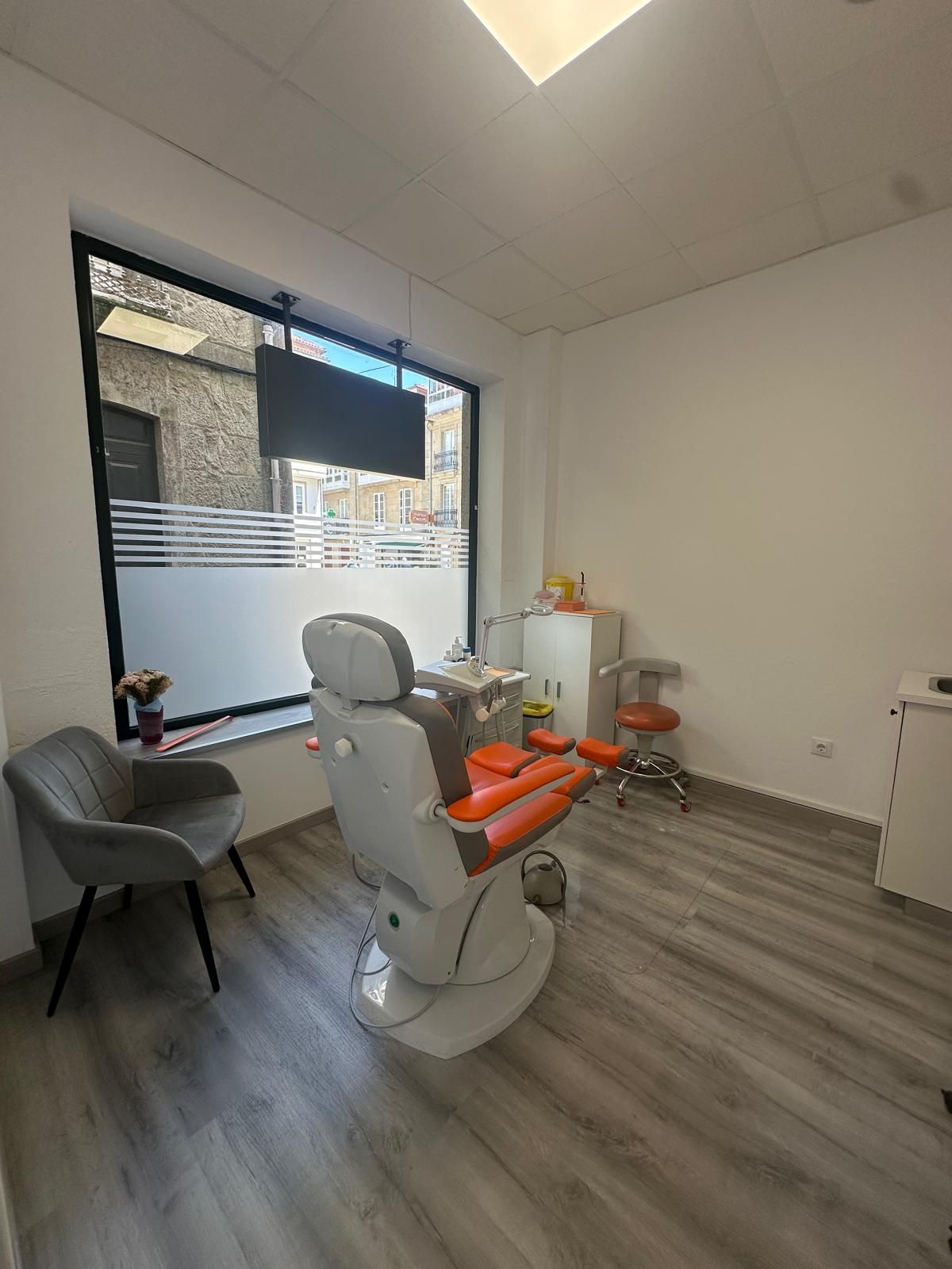 Gabinete con sillón podológico naranja junto a una gran ventana a la calle
