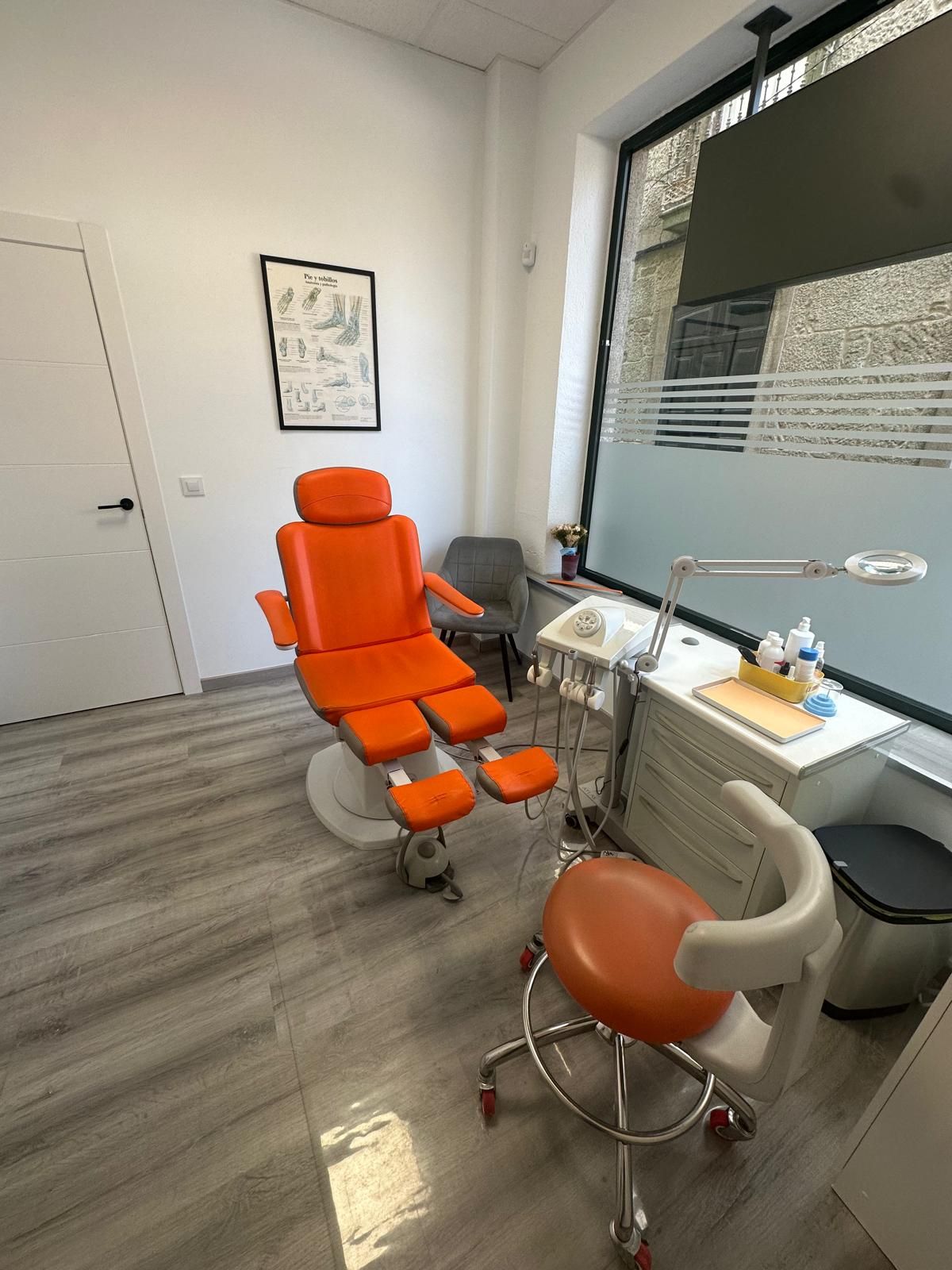 Sala de tratamiento con sillón podológico naranja, lámpara de aumento y carro de instrumental